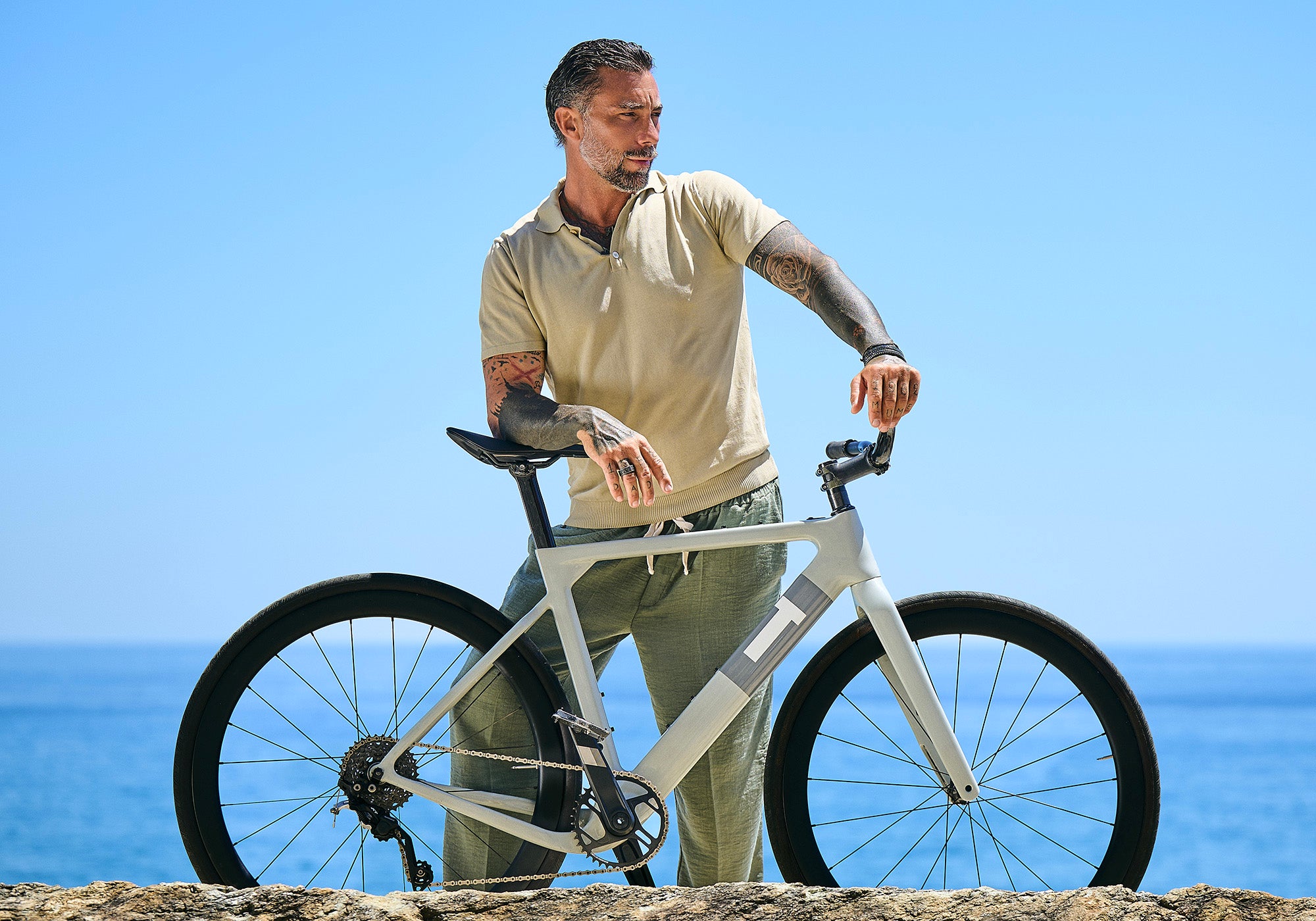Vittorio Brumotti avec son vélo sur un rocher au bord de la mer, portant les bijoux MANO Jewels en titane, or et diamants